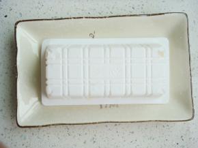 撕去豆腐盒表面的塑料膜，把豆腐盒子倒扣在盘子里，用剪刀在底部对角各剪开一个小孔。