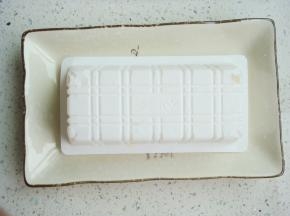 撕去豆腐盒表面的塑料膜，把豆腐盒子倒扣在盘子里，用剪刀在底部对角各剪开一个小孔。