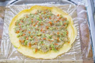 将面饼放在帘子上，摊上搅拌好的蔬菜鸡胸肉泥，然后卷起来。