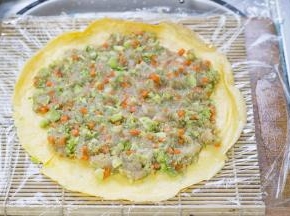 将面饼放在帘子上，摊上搅拌好的蔬菜鸡胸肉泥，然后卷起来。