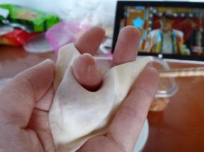 将云吞皮四边沾上少许水，将对角或对边折叠起来捏紧，并将中部收入。