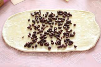 取出冷冻松弛好的面团，擀成长方形面片，刷一层蜂蜜，中间撒上的蜜豆，两头尽量少撒。