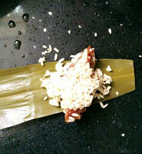 取一片粽叶，将粘着糯米的排骨捡一块上去