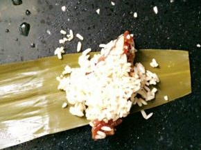 取一片粽叶，将粘着糯米的排骨捡一块上去