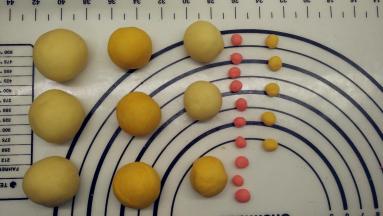 将黄色面团和红色面团揉均匀。预算好面团的大小。其中，鸡爸爸是原色面团，一只25g，三只共75g、鸡妈妈是黄色面团，一只20g，三只共60g，鸡宝宝两只原色，一只15g，共30g；一只黄色。因此，将所有的面团分好之后都滚圆备用。接着继续处理红色面团。分出10个1g的剂子，作为小鸡的嘴巴和头饰。黄色面团剩余的先分出5个1g小剂子，作为白色小鸡的嘴巴。