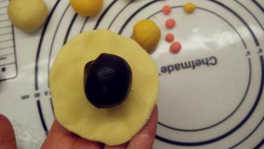 取出一个面团，将其压扁，形成中间厚四周薄的圆饼，在饼皮中间放上馅料。翻过来，将皮收一下，让它紧贴着馅料。