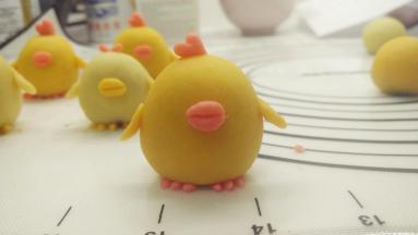 接着取个1g的红色剂子，将它分别整形成椭圆形状，再用牙签在中间压一下，做成小鸡的嘴巴，贴在面团中间。再取一个黄色小剂子，压成圆形之后用剪刀剪成两半，再分别剪两刀（不要剪断），变成山字形，整形成小鸡的脚。最后用红色小剂子做成爱心,贴在小鸡头顶,当做装饰.这样一只小鸡的造型就做好啦。