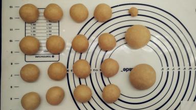 发酵好的面团用擀面杖排气，先分割出一个48g的面团（做耳朵），一个64g的面团（做手脚），以及一个5g的面团（做眉毛）。剩下的把它们均分成16份做泰迪熊的头和身体。将它们都滚圆之后盖上保鲜膜松弛15分钟。