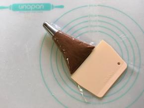 将做好的可可淡奶油曲奇面糊装入裱花袋中，用刮板辅助将面糊刮入排除空气