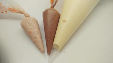 舀出1勺面糊，加入红曲粉，翻拌均匀。再舀出1勺，加入可可粉，一样翻拌均匀。这样我们就得到了3个颜色的面糊，分别将它们装进裱花袋中。