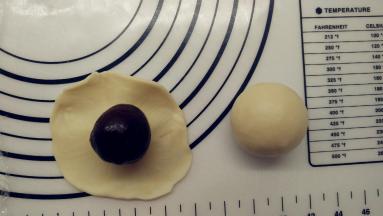 接着放上包好的豆沙蛋黄馅。翻过来，将皮收一下，让它紧贴着馅料。一手大拇指按住馅料，另一手虎口往上推饼皮，使它紧贴着馅料并慢慢地往上爬，最后收口，收口一定要收紧。