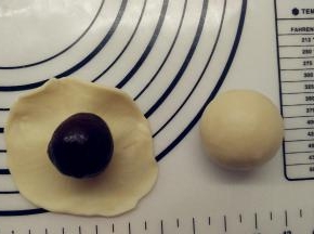 接着放上包好的豆沙蛋黄馅。翻过来，将皮收一下，让它紧贴着馅料。一手大拇指按住馅料，另一手虎口往上推饼皮，使它紧贴着馅料并慢慢地往上爬，最后收口，收口一定要收紧。