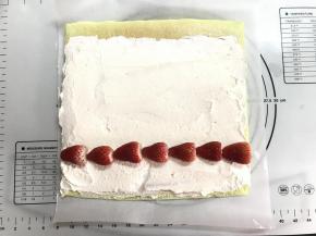 等蛋糕体完全冷却后，将蛋糕翻面并撕掉底部油纸，如果毛巾面卷外面，那就再将蛋糕体翻过来放在干净的油纸上。淡奶油加入10克全脂奶粉及10克糖打发到偏硬状态，抹在蛋糕表面，起始端稍厚，尾部稍薄并留2-3厘米不要抹奶油，放上草莓。