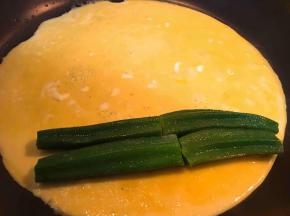 蛋液二分之一倒入平底锅中，未凝固时放入煮熟的秋葵，借助铲子和手，从边缘卷起。