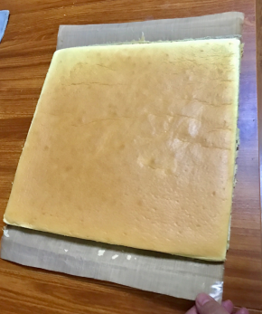 取出后，震摔一下去掉热气，然后从烤盘拿出来。晾一分钟，然后表面放个物件，帮忙把蛋糕卷翻过来，趁热撕掉油纸