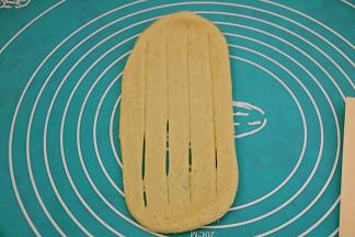 取一个面团用擀面杖，擀成椭圆形，翻面用刮板在面团中间切四刀，下方的面团底边压薄。