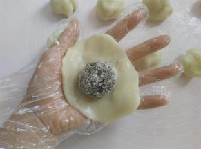 取一个面团压扁，包上豆沙馅，像包包子那样包起来，捏一下收口