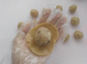 戴上一次性手套，取其中一个面团用2个掌心的摩擦力按扁，放上五仁馅