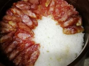 待米饭煮至锅内已无水冒泡后，放入切成片的腊肠，继续小火焖