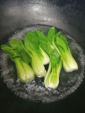 这时候我们可以把三颗小油菜对半切开，在开水里烫熟