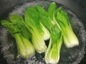 这时候我们可以把三颗小油菜对半切开，在开水里烫熟