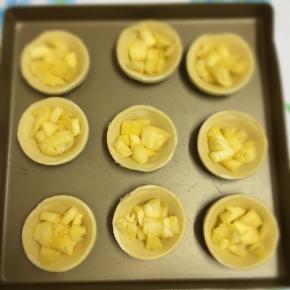 将挞皮码放在烤盘里，加入腌好的菠萝丁。