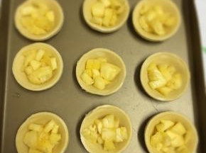 将挞皮码放在烤盘里，加入腌好的菠萝丁。