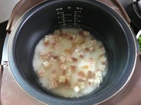 3、把淘洗干净的大米倒入电饭煲中，加入适量水，再把切丁的腊肉一起加入后拌匀，开始煮饭。