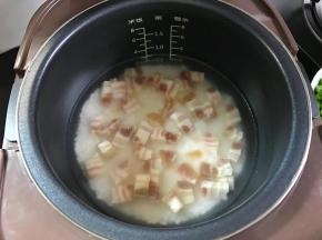 3、把淘洗干净的大米倒入电饭煲中，加入适量水，再把切丁的腊肉一起加入后拌匀，开始煮饭。