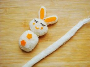 小花朵点缀身体部分，米饭放入保鲜膜里捏紧搓细长条，待会做小兔子的手臂和腿部。