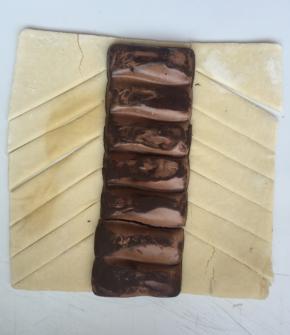 准备一张酥皮，放上巧克力，切成斜条，左一片右一片左一片右一片这样压住（后面我用火腿肠分解动作）