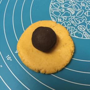 取一份面团按扁，包入称量好的豆沙，捏紧收口。