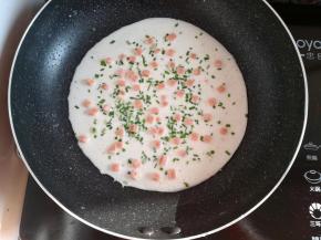 在面糊上撒上适量的野葱碎和火腿肠丁，开小火煎饼