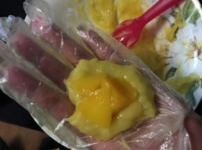 准备一碗水，一个一次性手套，这个方法是小编试过最好用的了，戴好手套，抹一点点水，然后抓一点点糯米面注意烫伤，然后中间塞一个芒果肉，然后用勺背压一压这个芒果肉，压进糯米面里，然后右手也要少沾点水，因为糯米面实在太黏了，像包包子一样包好，左手倒右手，右手倒左手，撮圆了