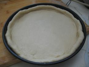 披萨盘上摸油，将擀好的面皮放入批萨盘内，用手按压面皮，把面皮撑至与盘子同样大