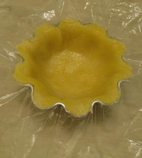 将面团用擀杖擀开，连同保鲜袋一起放在蛋挞模具里压出形状