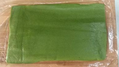 剩余的抹茶面团搓成21CM长条，套上保鲜袋擀成中间稍厚，两边薄的片状，宽度以完全包裹住步骤14的面团为准。
