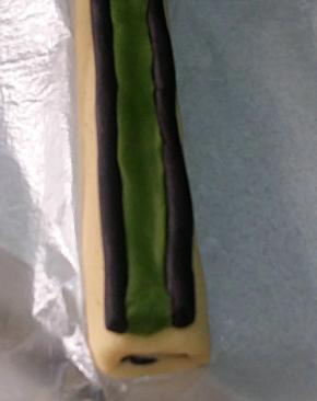 取剩下的两份11克可可长条（耳朵），放在步骤13的面团顶部两侧 ；
取15克抹茶面团，搓成21CM长条，稍稍按扁，放在两条可可长条中间。将可可长条跟抹茶长条捏紧，不留缝隙。此时可将面团冷冻一至两分钟，为下步抹茶面团包裹时不变形做准备。