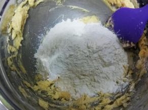 把过筛后的低粉倒入打好的黄油中，用刮刀翻拌均匀，捏成面团。