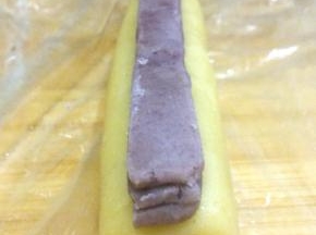 将抹茶面团切出三个1CM的长条，叠放在椭圆面团中央，用保鲜膜将两种面团压实弄平整；