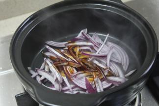 拿出砂锅，开火加热并将洋葱洗净切好，放入锅底一起烧，加入美极鲜