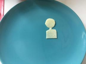 苹果切薄片，剪成小男孩身体和头的形状摆到餐盘合适的位置上。