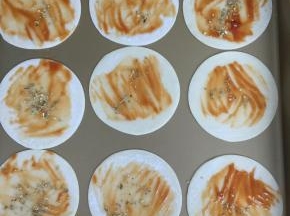 将饺子皮码放入不粘烤盘中，刷番茄酱，撒上少许披萨草。