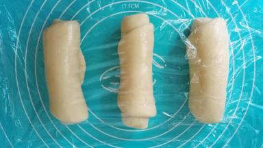 取一个面团，用擀面杖擀成牛舌状，然后翻过来，从下往上卷起，三个全部卷好后用保鲜膜盖好继续松弛10分钟