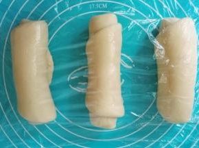 取一个面团，用擀面杖擀成牛舌状，然后翻过来，从下往上卷起，三个全部卷好后用保鲜膜盖好继续松弛10分钟