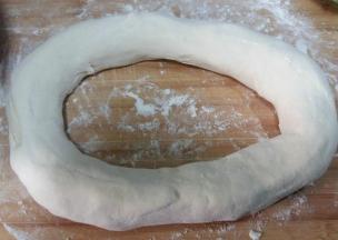 拿走擀面杖，两手顺洞口把面团向外抻长。从中间切断。