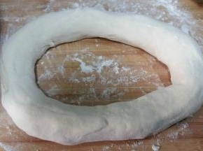 拿走擀面杖，两手顺洞口把面团向外抻长。从中间切断。