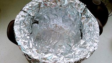 另一张锡纸也放入锅内，十字交叠成直筒状，一圈贴牢砂锅内壁，顶部包住砂锅边沿。