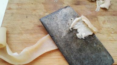 把猪皮放案板上，逐片用刀刮净背面的肥油。