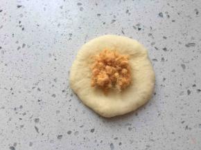 取一个松弛好的面团，按扁，拍掉周围气泡，边缘压薄些，包入适量肉松